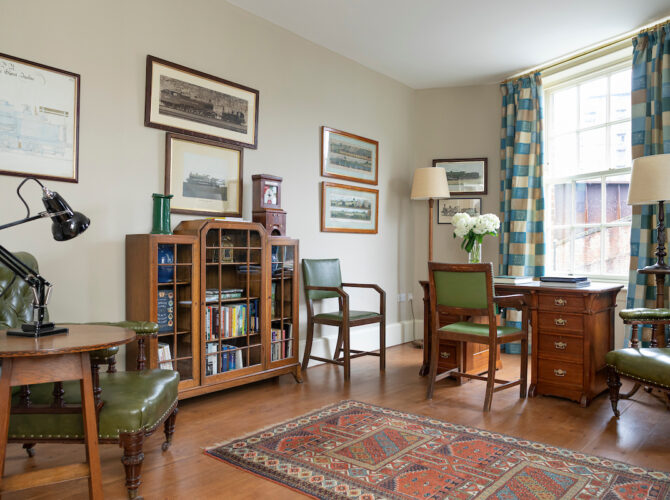 Interior study with wooden furniture, bookshelves, and framed prints, reflecting a traditional domestic setting.