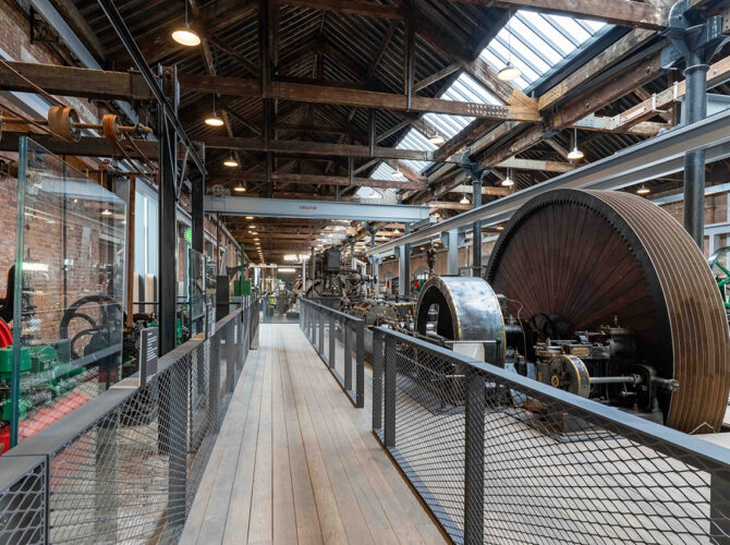 Close view of a massive stationary engine with a prominent flywheel, displayed alongside other historic machinery.