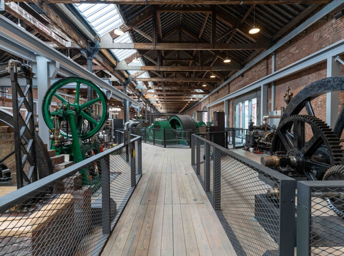 Perspective view down the exhibition space showing multiple engines aligned along a central walkway within the restored industrial hall.