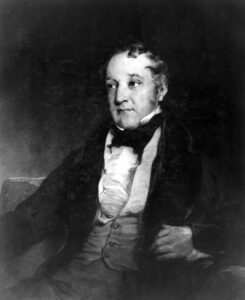 Image of William Huskisson M.P sat in a chair with curly black hair and wearing a victorian dress suite.