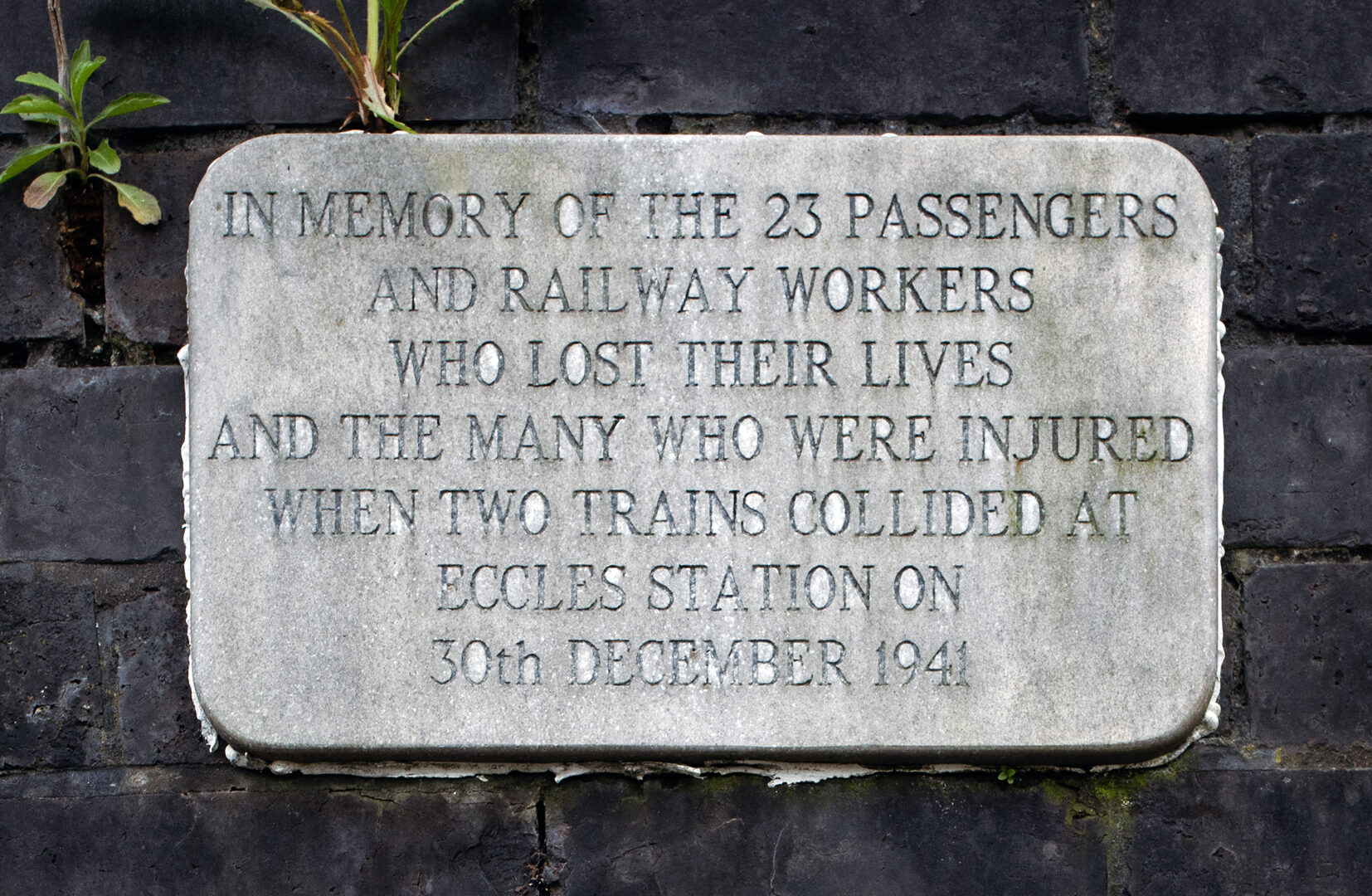 Stone plaque on a dark brick wall, with text commemorating the rail crash