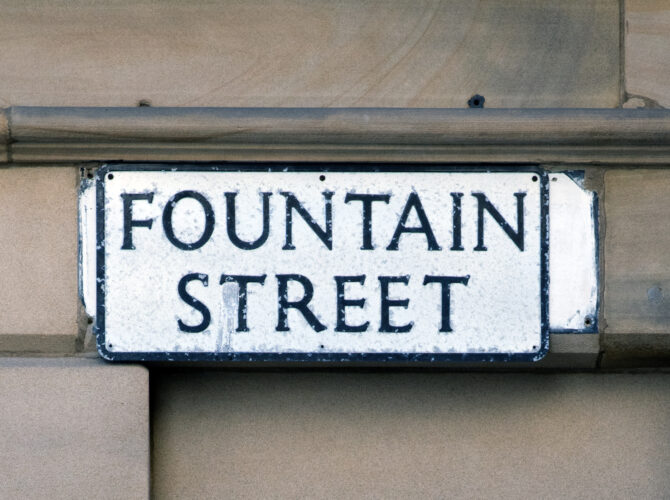 Close-up of a classic street sign fixed to a stone building, displaying the name Fountain Street in bold black lettering.