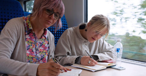 Two women sat on a train writing in books