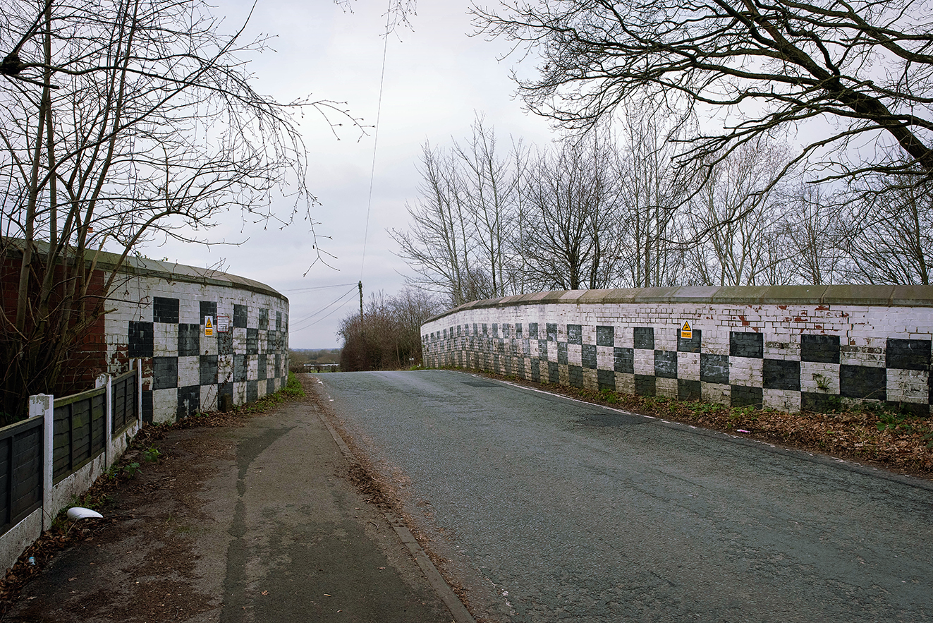 A broad view across the top of Broseley Bridge, with the chequered parapets extending on both sides of the road. The perspective emphasises the bridge’s scale and its continued use as a local route.