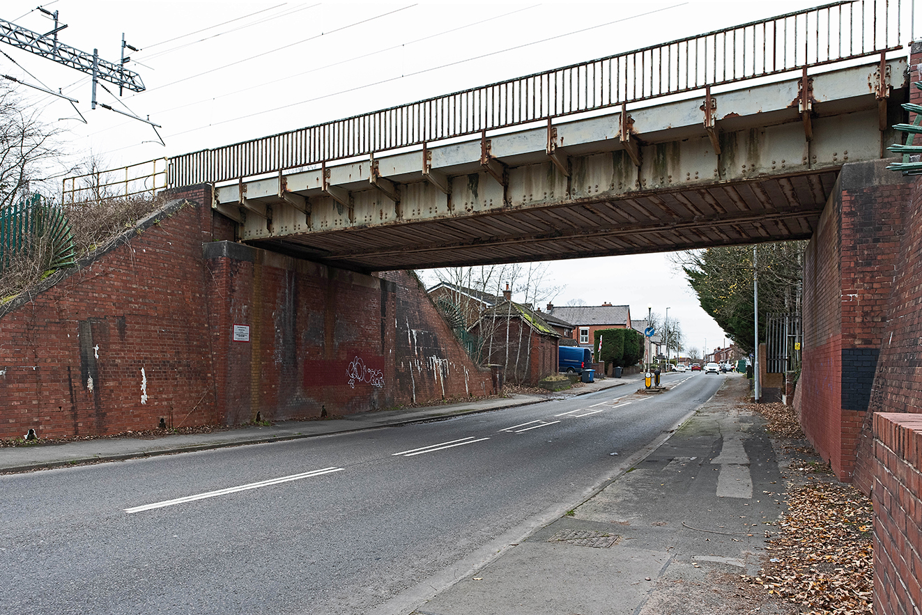 A rebuilt railway bridge with steel girders and brick abutments carrying the line over Warrington Road, marking the historic crossing point.