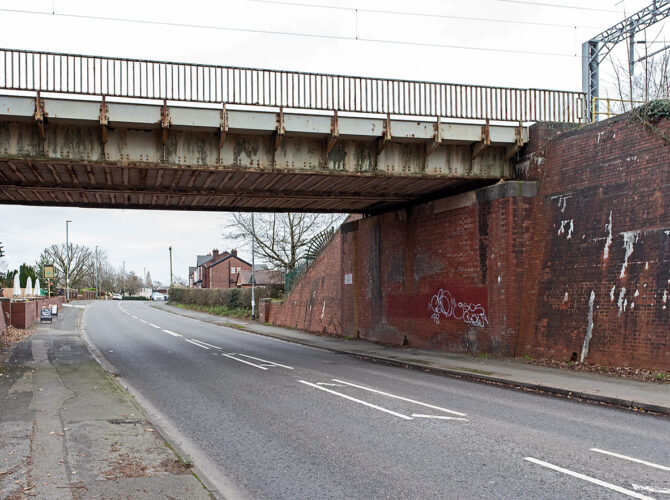 The underside of the bridge showing weathered steel beams and brick supports as the road passes beneath, highlighting later alterations to the original structure.