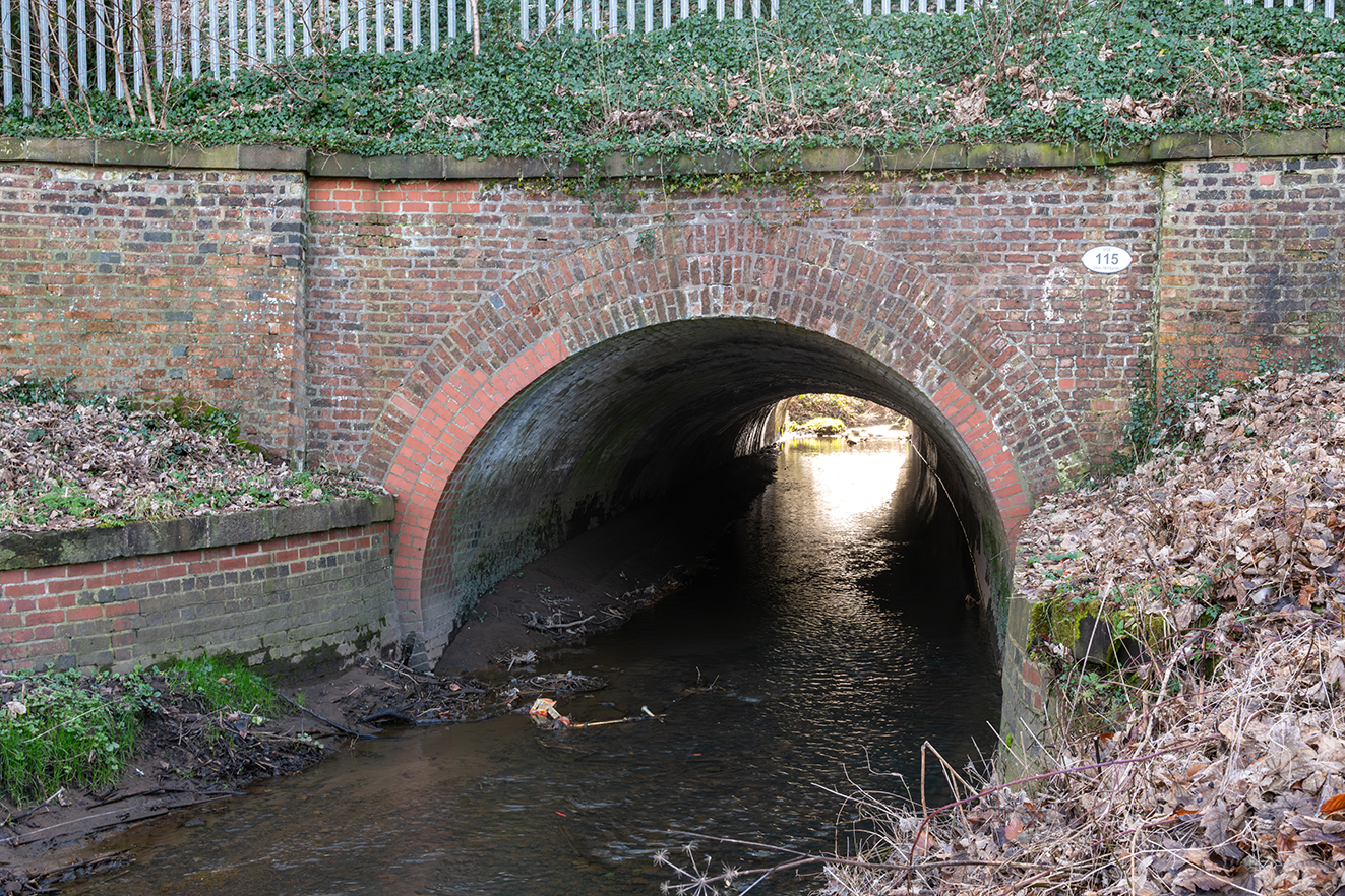 Looking through the culvert, the arched brick lining frames the flowing water and light beyond.