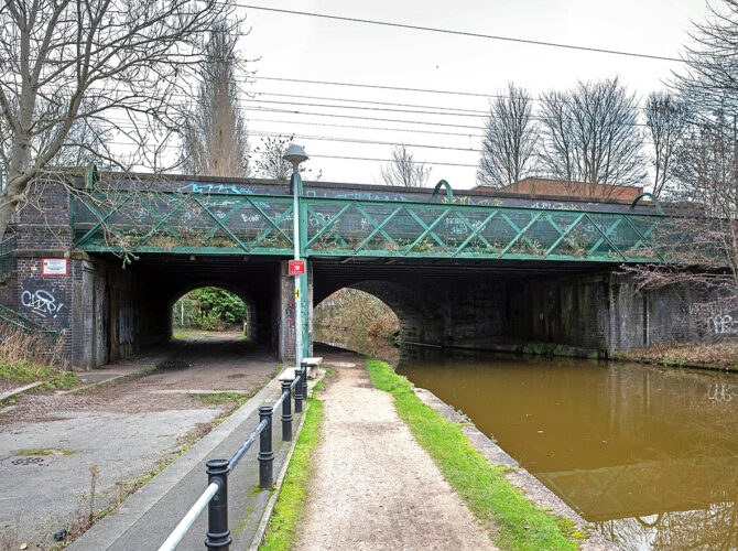 Narrow towpath and canal running beneath the bridge’s stone and iron structure.