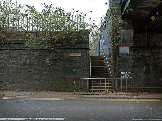 Stairway rising beside the bridge wall from the roadside to track level.