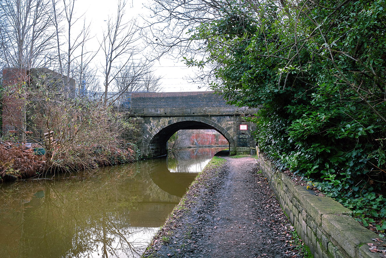 Calm canal water reflecting the curved stone arch and surrounding greenery.