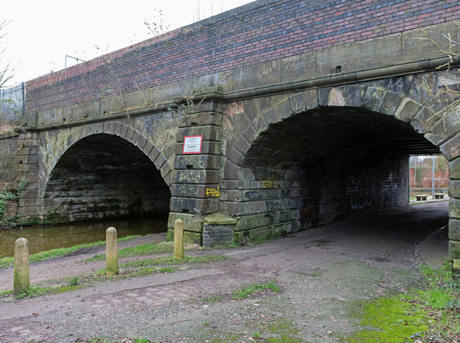 Sandstone bridge with two arches carrying the railway above the canal and towpath.