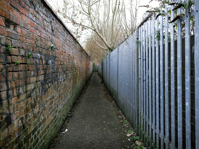Straight walkway bordered by brickwork and metal fencing near the railway.