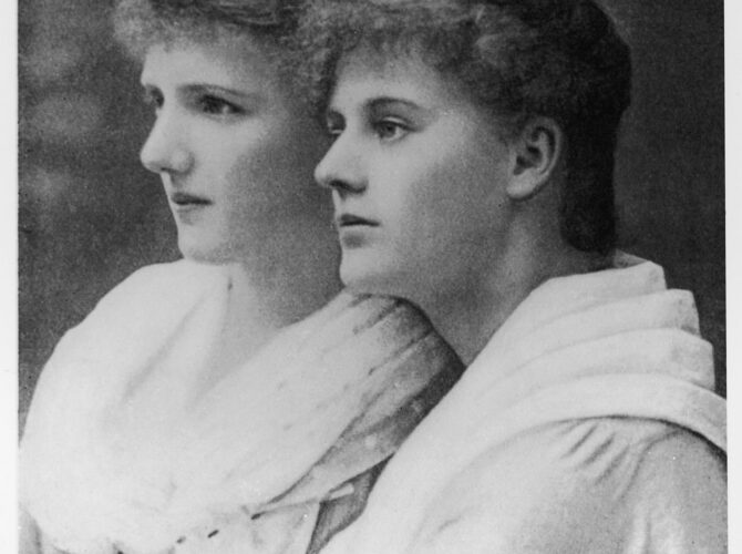 A black-and-white portrait shows sisters Eva Selina Laura Gore-Booth and Constance Gore-Booth seated side by side, both in profile. Dressed in late 19th-century attire with high collars and carefully styled hair, they appear calm and composed, reflecting the formal style of studio photography of the period.