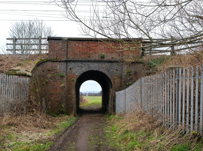 A straight-on view of the brick arch bridge with a dirt track leading through to open fields beyond.
