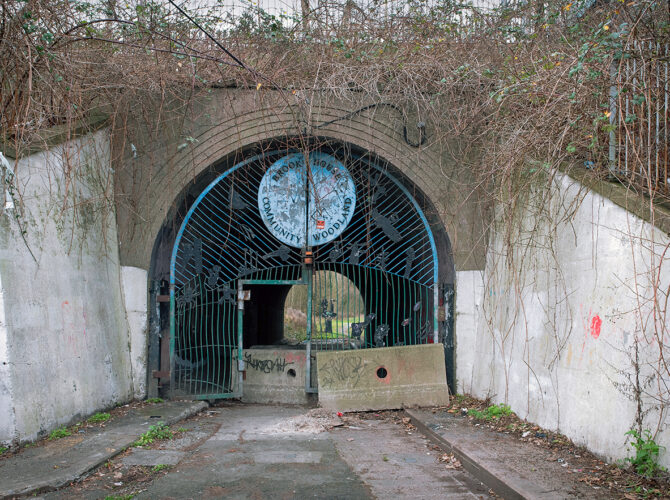 The brick arch entrance framed by vegetation, with a metal gate featuring artwork for Brook House Community Woodland.