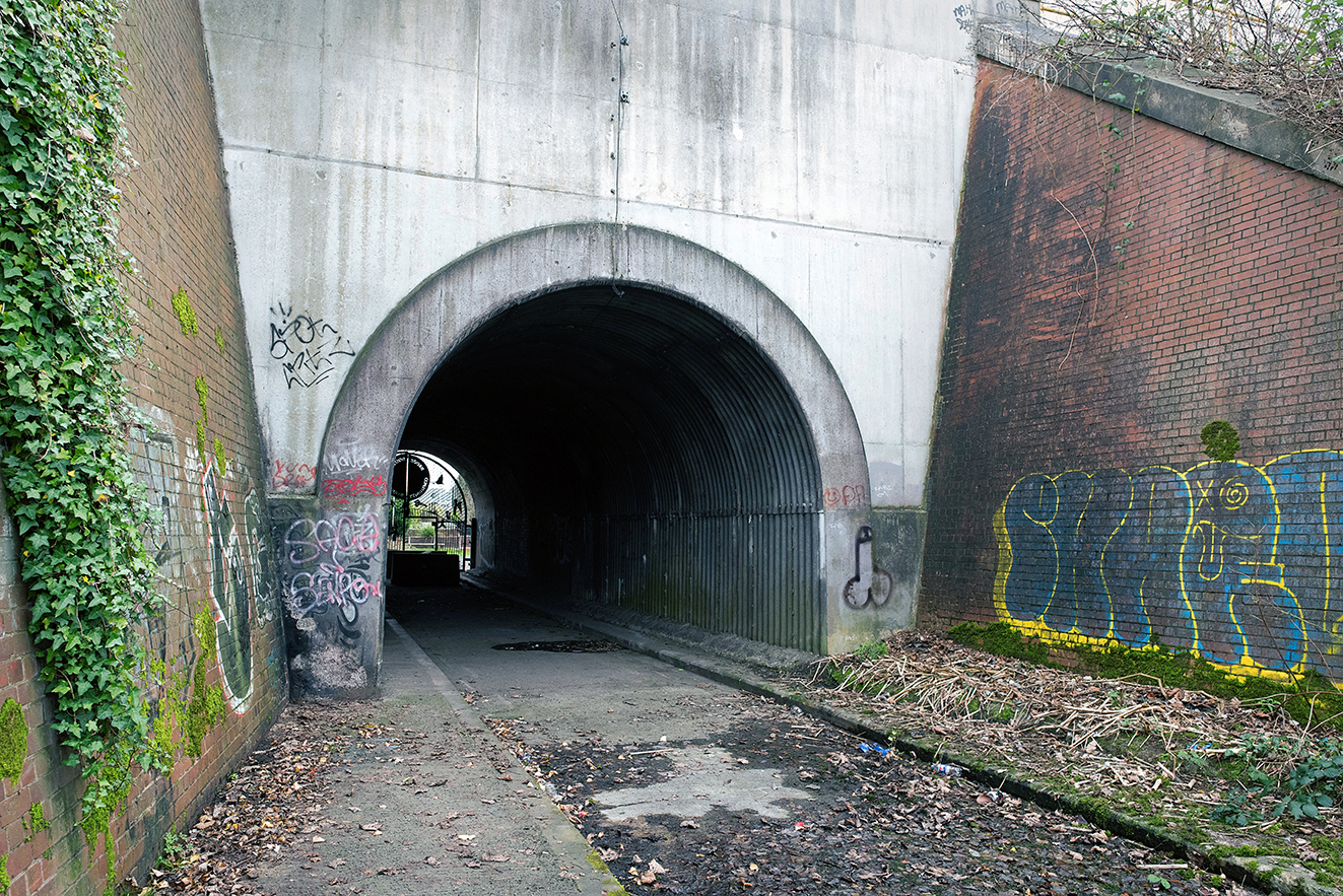 A wider view showing the tunnel entrance set within later concrete and brickwork, with signs of modern use and graffiti.