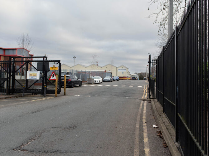A view through security gates into the business park, showing access roads and light industrial units.