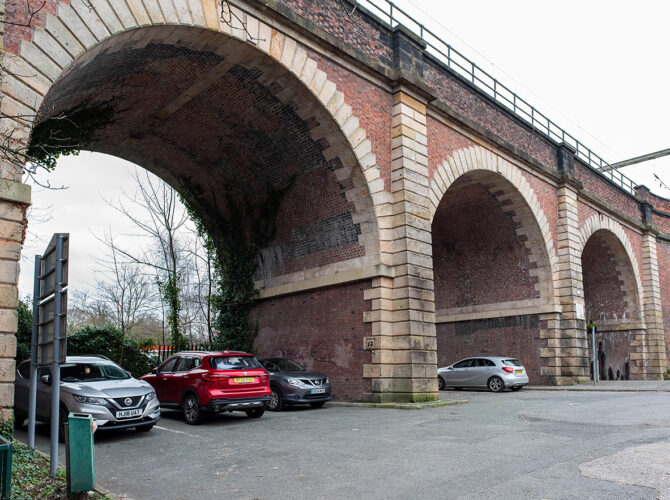 Angled view beneath the arches highlighting brickwork, stone detailing and cars parked under the structure.