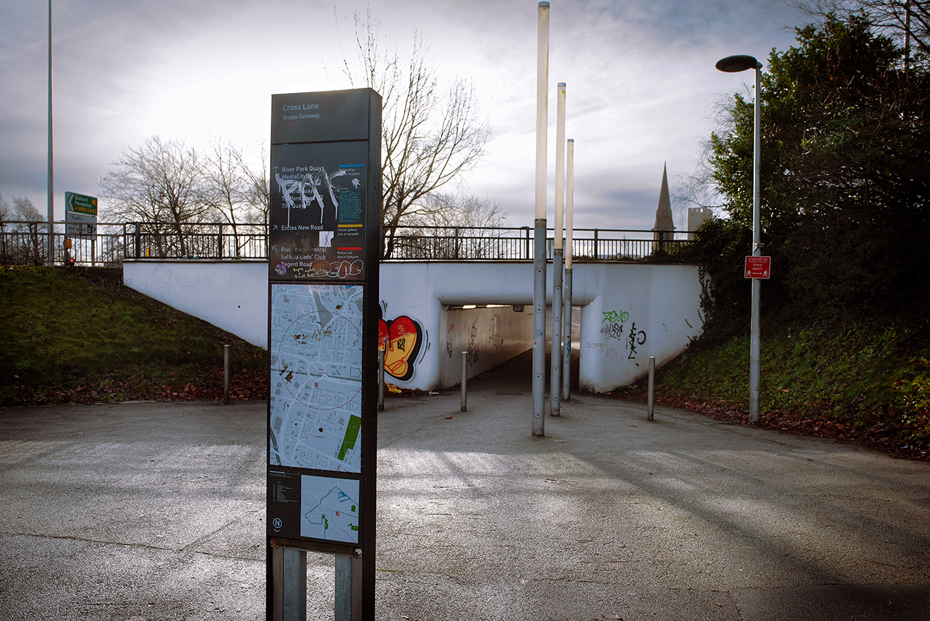 Information sign standing in front of the underpass entrance, showing local directions and map, with the road and rail bridge above