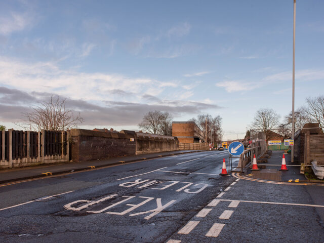 View of the road approaching the crossing with painted markings and traffic cones in place