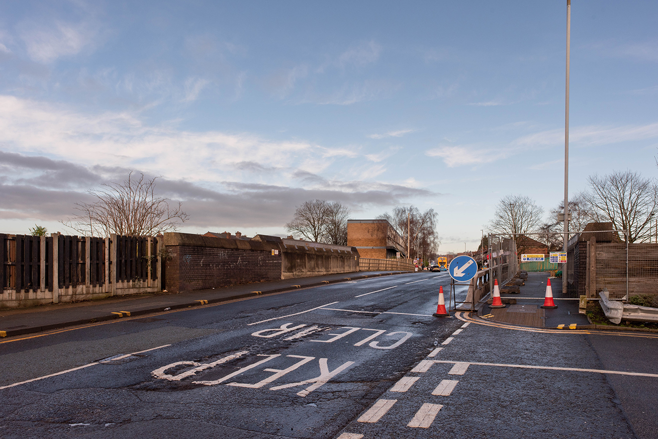View of the road approaching the crossing with painted markings and traffic cones in place