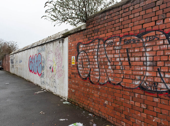 Close view of mixed brick and concrete wall covered in graffiti, showing the contrast between older brickwork and later concrete sections along the street