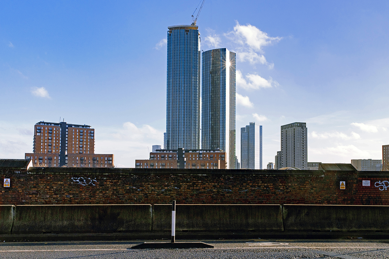 Tall glass buildings stand beyond an older brick railway wall showing contrast between eras