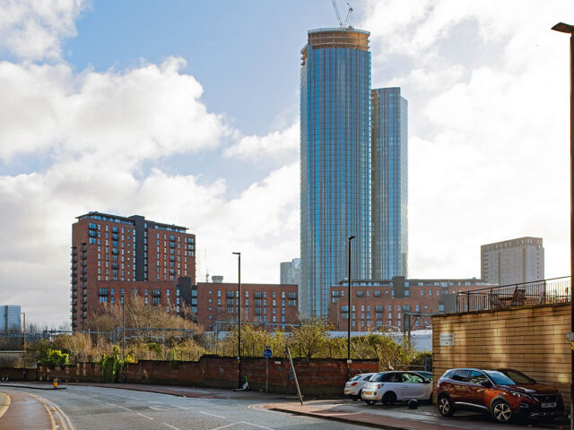 Wide view of the street and wall with high-rise buildings beyond, showing old and new together.