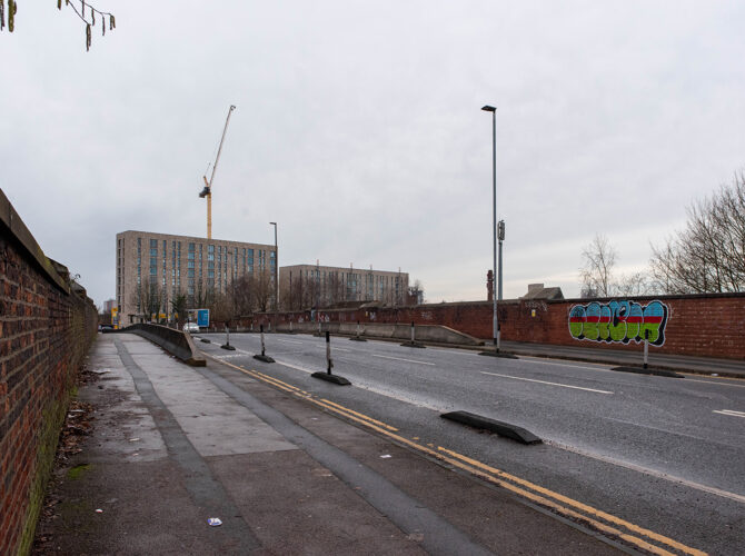 Wide road flanked by brick railway walls and modern buildings