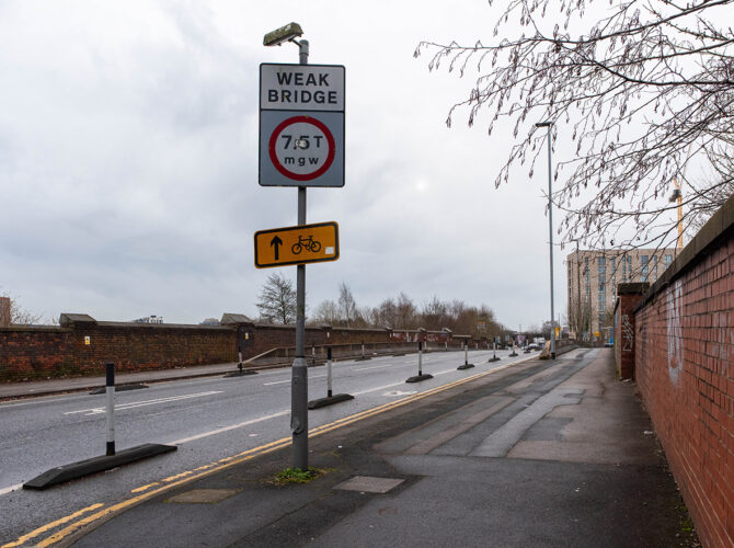 View down the road with weight restriction sign and continuous brick wall lining the route