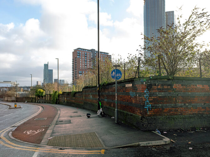View along Ordsall Lane with the historic wall and Manchester skyline rising behind.