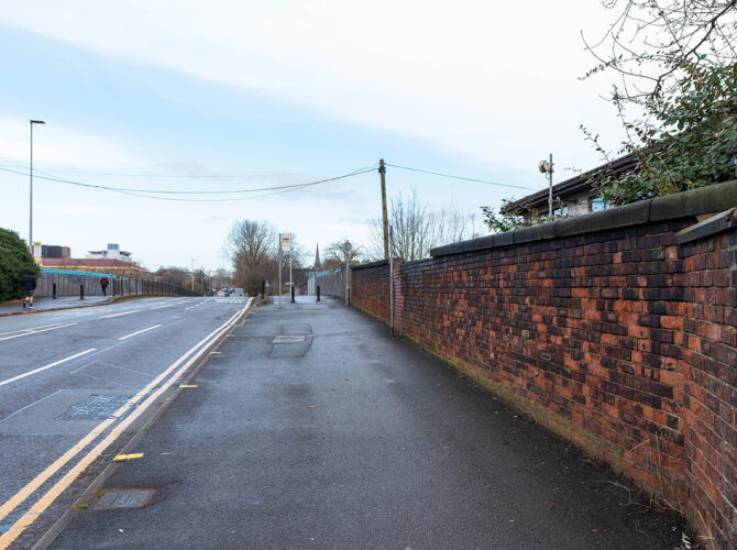 View along the roadside showing boundary walls and the gradual rise of the bridge.