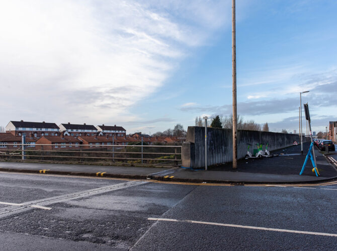 Wide view of the road crossing the railway cutting, with metal railings and a junction in the foreground