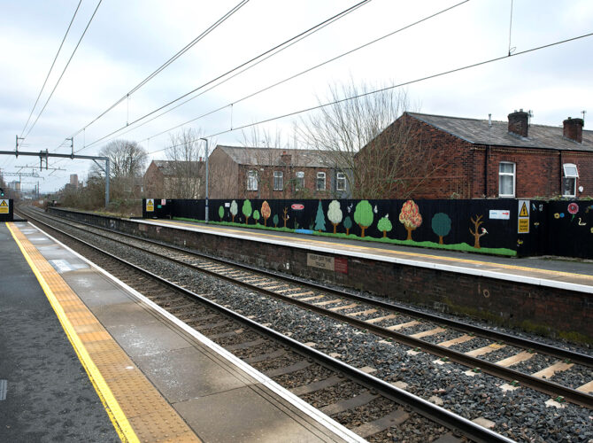 The railway line beside the platform, with terraced houses and painted fencing in the background.