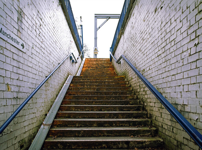 A stairway rising from the underpass to platform level, lined with white brick walls.