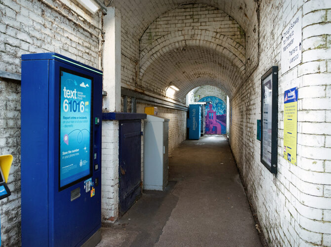 A white-painted brick subway beneath the tracks, with a curved ceiling leading between platforms.