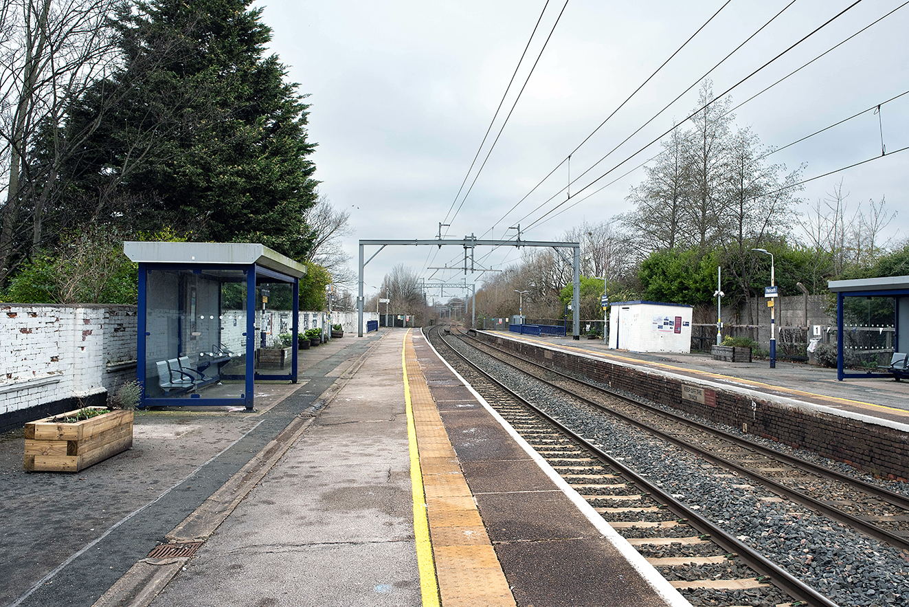 A wide view of the platforms, showing waiting shelters, planters and electrified railway lines.