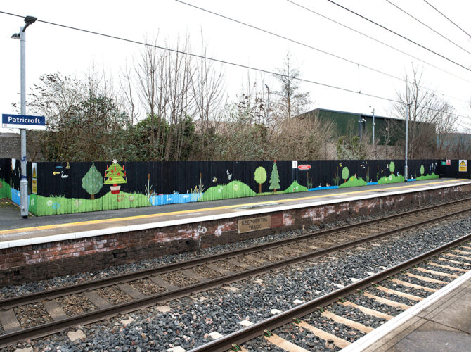 A colourful mural of trees and wildlife along the fence beside the opposite platform.