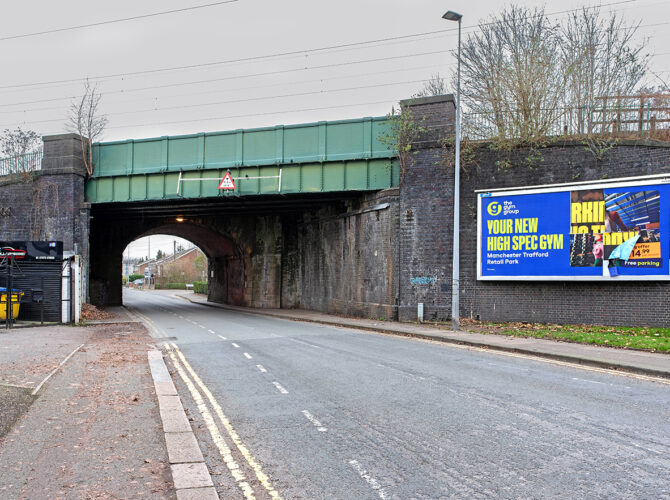 A wide street view showing the historic bridge, where a modern green steel deck sits above an earlier brick arch structure.