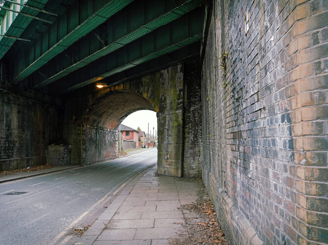 A closer look beneath the bridge reveals heavy steel girders overhead and the older brick arch lining the roadway.
