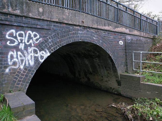 A close view of the culvert entrance where the brook flows under the brick arch beneath the embankment.